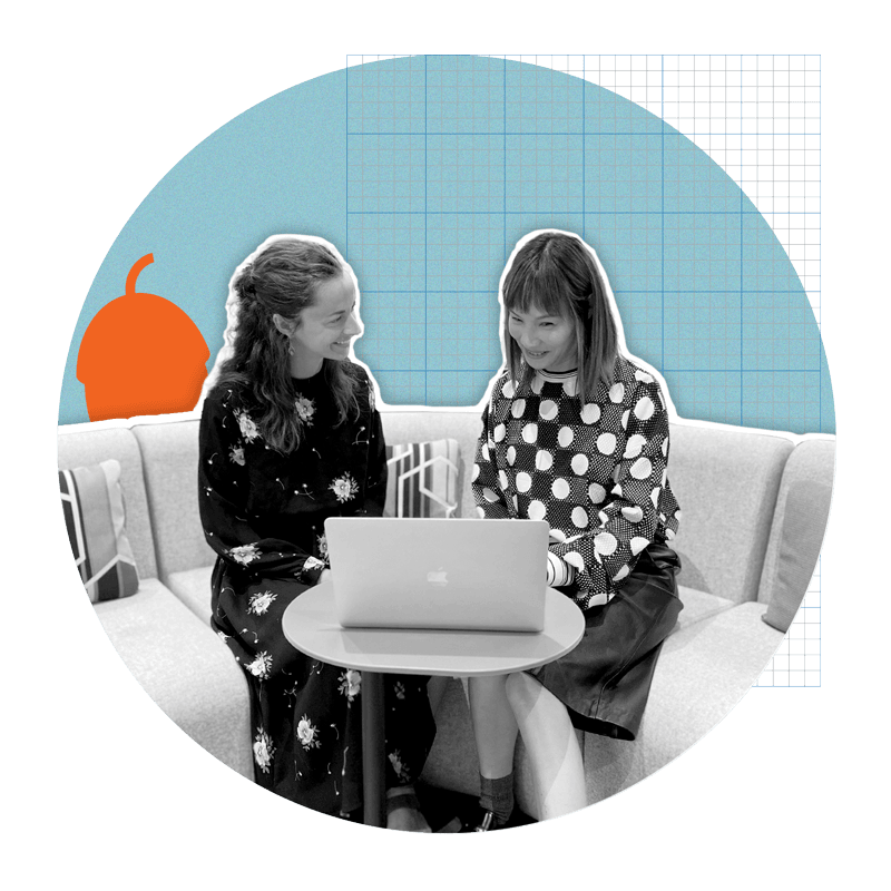 Two young women sitting on office couch, looking at laptop